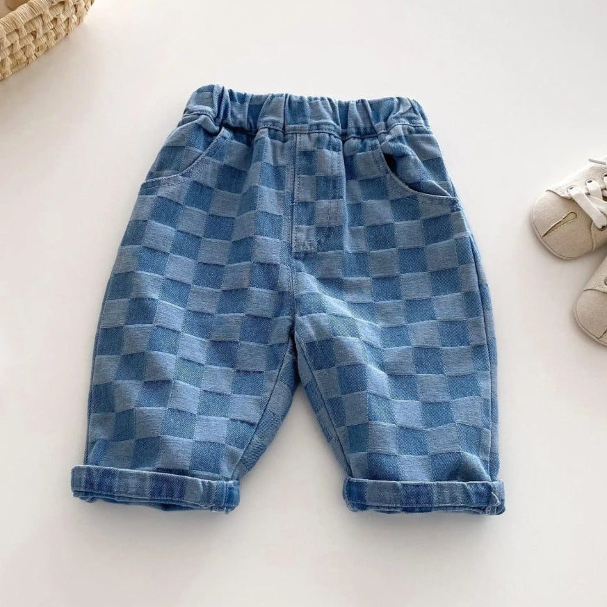 Blue checkered pants on a white surface with a book and shoe in the background