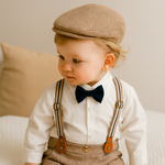 Child wearing a formal outfit with suspenders, bow tie, and flat cap on a neutral background