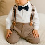 Child wearing a formal outfit with suspenders, bow tie, and cap on a neutral background